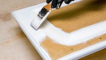 Hand holding a paint brush, painting a cabinet door white