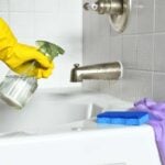 Human hand in a yellow glove using spray bottle to clean a bathtub