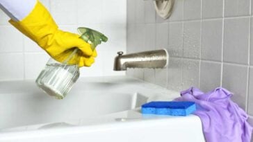 Human hand in a yellow glove using spray bottle to clean a bathtub