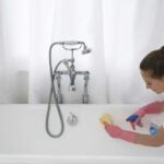 Woman leaning into white bathtub with cleaner and a rag to clean the tub.