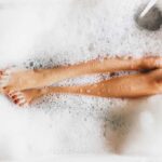 Overhead view of legs peaking through bubbles in a bathtub