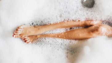 Overhead view of legs peaking through bubbles in a bathtub