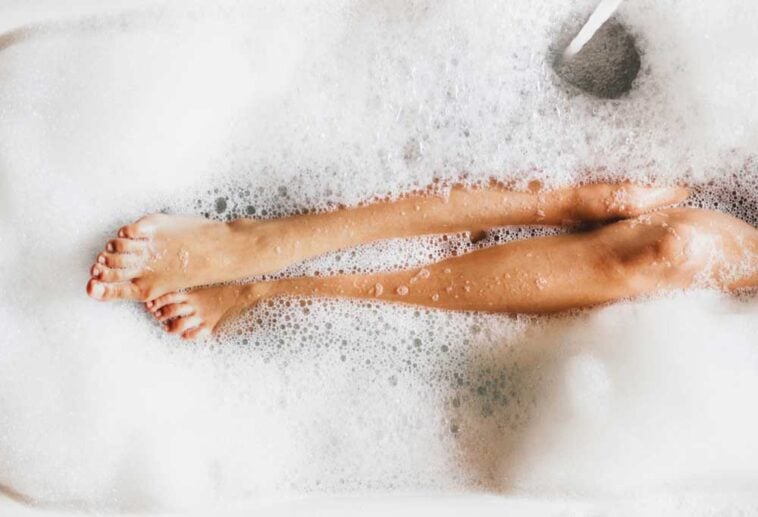 Overhead view of legs peaking through bubbles in a bathtub